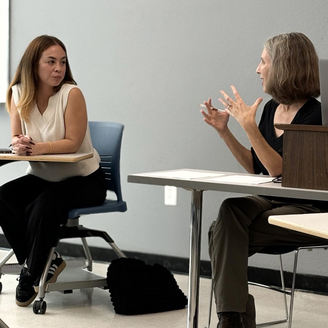 Humanities MA alum Caitilin Damacion and Cristina Ruotolo mid discussion in a classroom