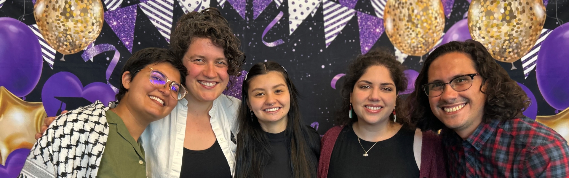 Five Humanities and CWL students smiling in front of a gold, black, and purple photo banner