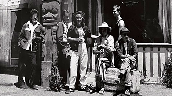 Black and white photo of 6 people standing and sitting outside a building